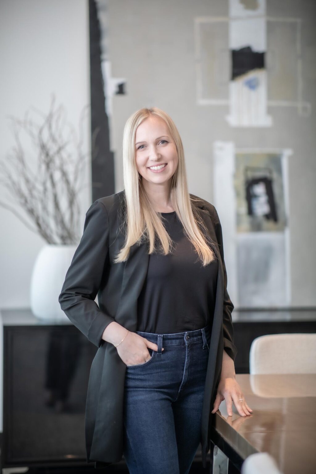 Alix Rios, Associate Principal and Studio Director at GFF, standing in a modern conference room with abstract artwork and neutral decor, wearing a black blazer and jeans.