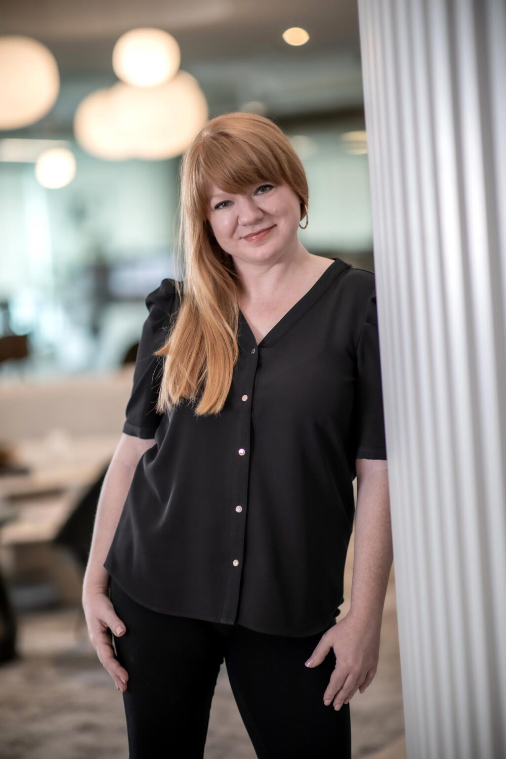 Emily Mendez, Associate and Director of Sustainability at GFF, leaning against a column in the office wearing a black blouse.