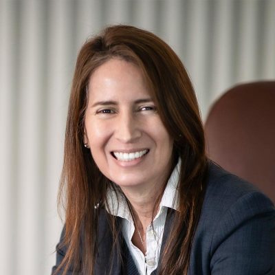 Maria Gomez, AIA, LEED AP, Principal and Studio Director at GFF, close-up portrait smiling in a navy blazer with soft office background.