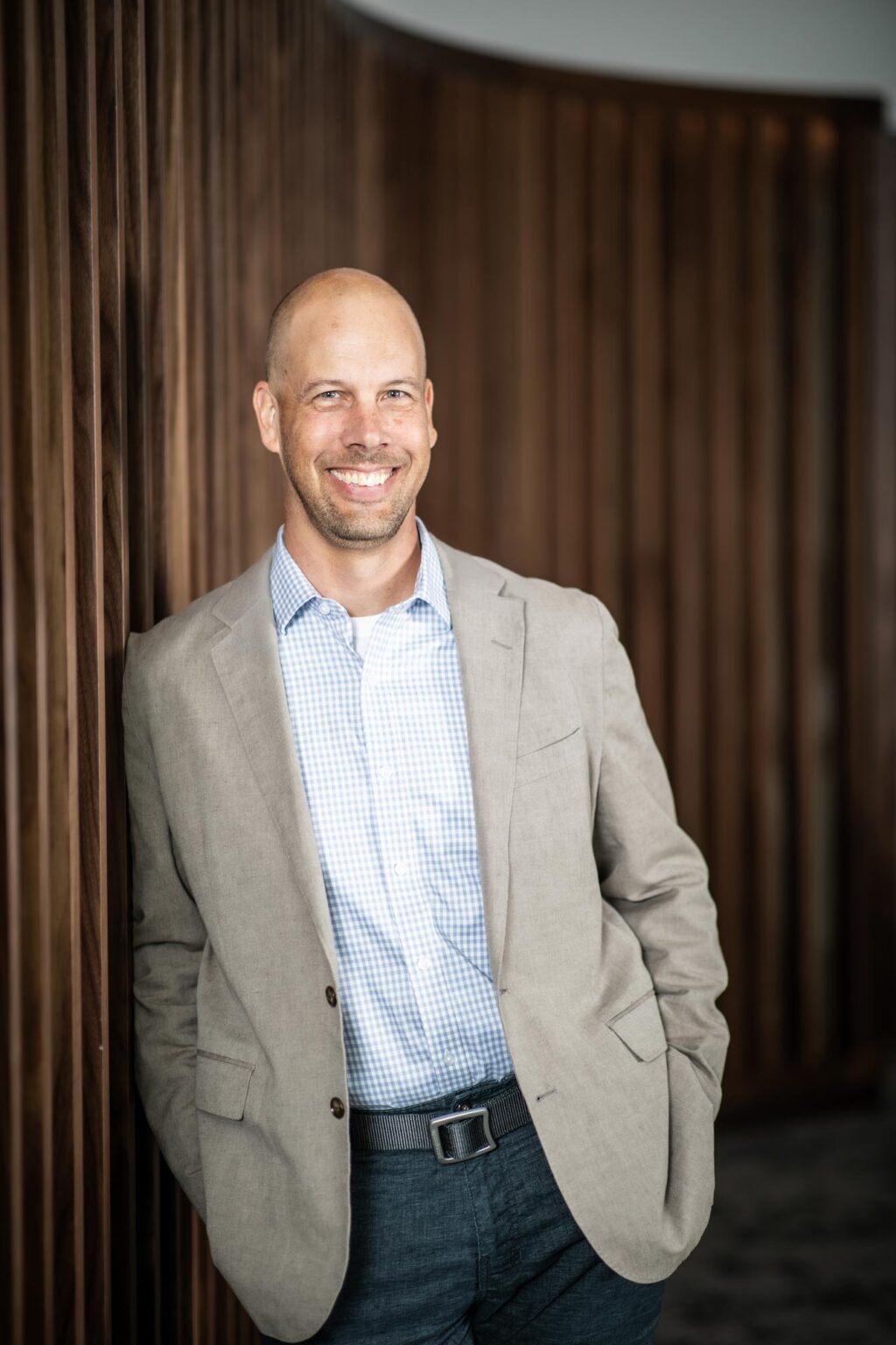 Aaron Hunt, AIA, Associate Principal and Managing Director at GFF, standing against a wood-paneled wall in a light blazer and checkered shirt.