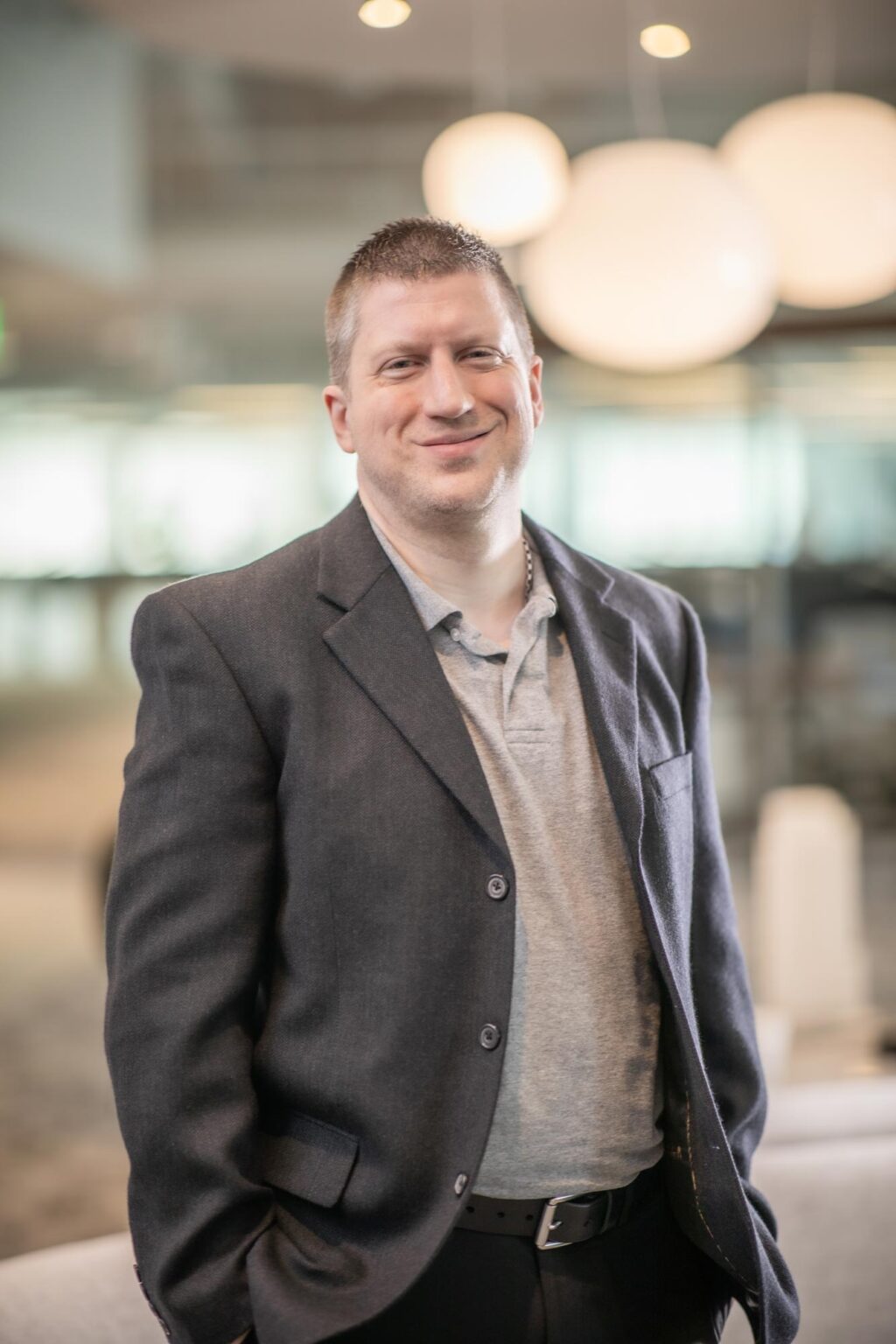 Phil DeLaughter standing in a bright modern office environment, wearing a gray blazer and polo shirt, smiling at the camera.