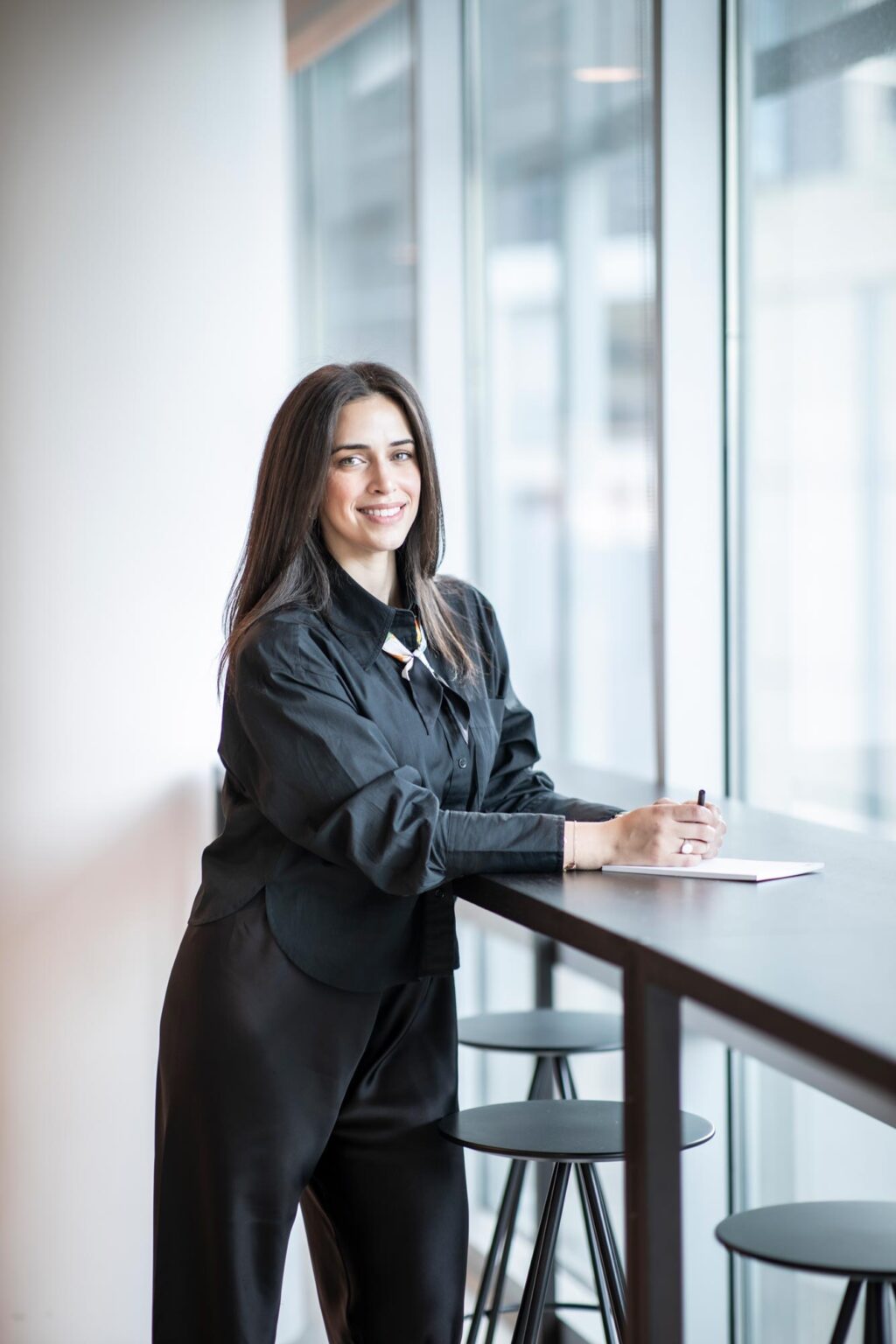 Dina Otrok, architect and interior designer at GFF, photographed in a modern Dallas workplace interior, standing at a tall desk with natural light.