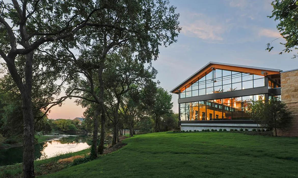 Exterior view of Hasley Chapel at sunset, featuring large glass windows reflecting the natural creek and trees.