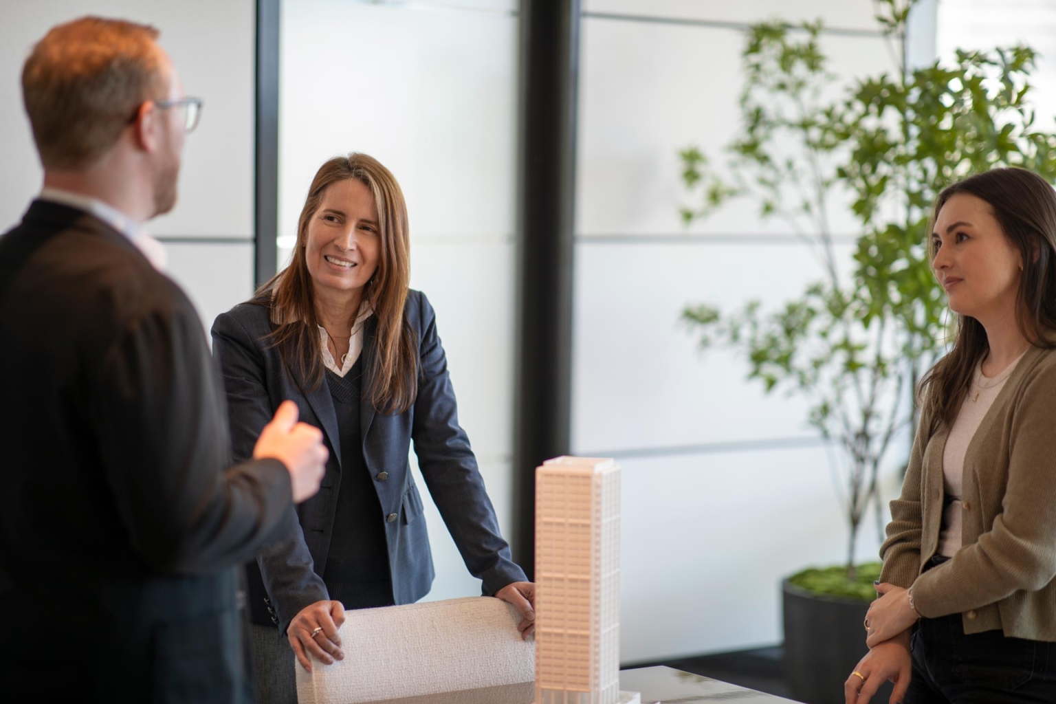 Architect standing at a table in discussion with colleagues, architectural model in foreground.