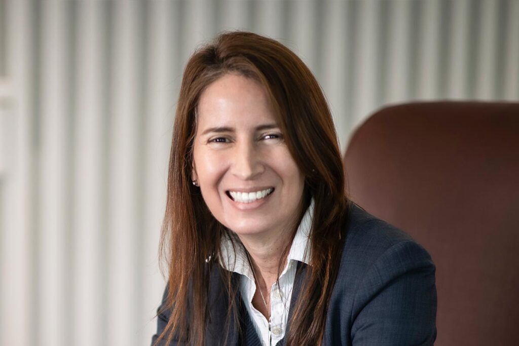 Maria Gomez, AIA, LEED AP, Principal and Studio Director at GFF, close-up portrait smiling in a navy blazer with soft office background.