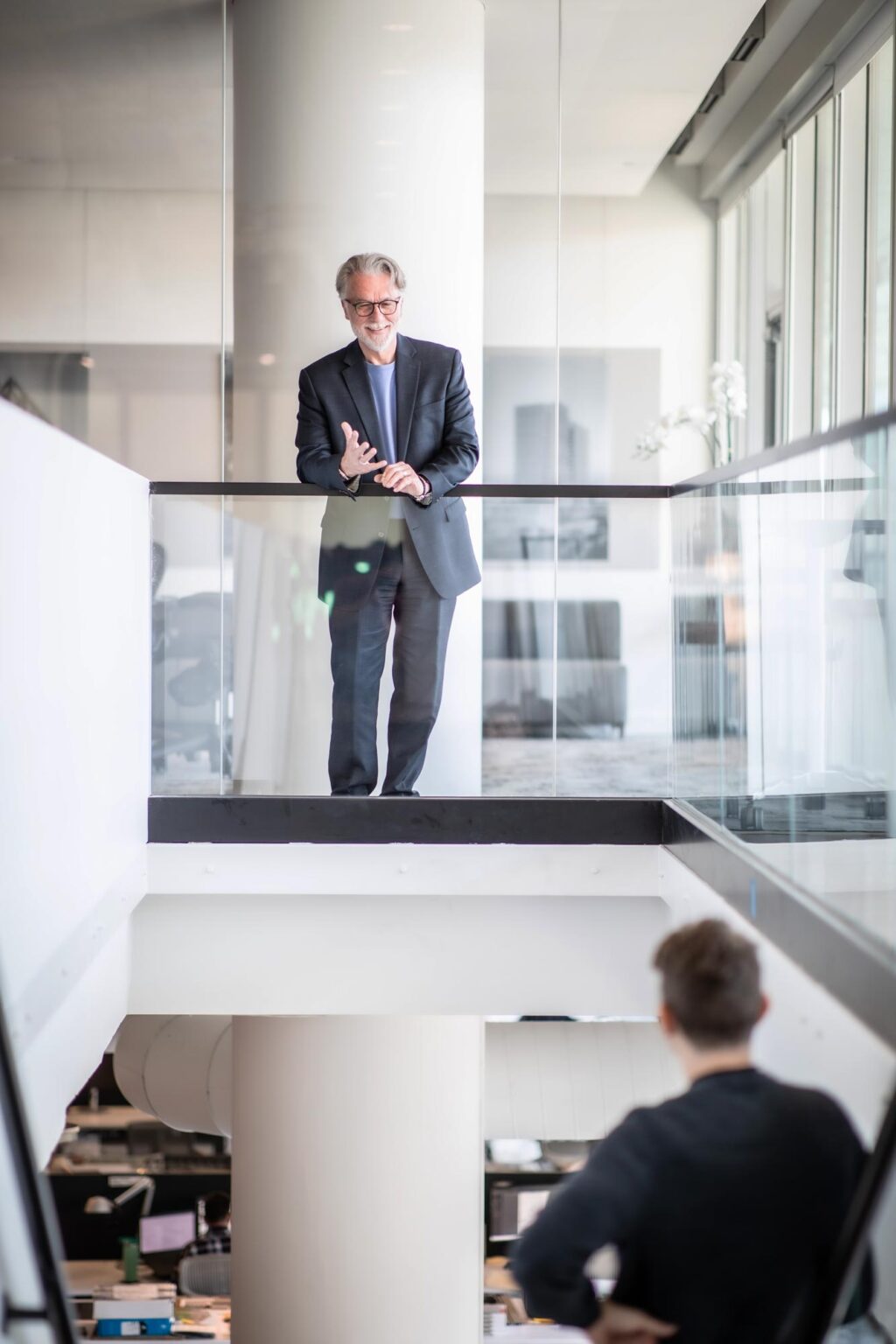 Brian Kuper standing on a glass balcony in GFF’s office, speaking to a colleague below while smiling and gesturing.