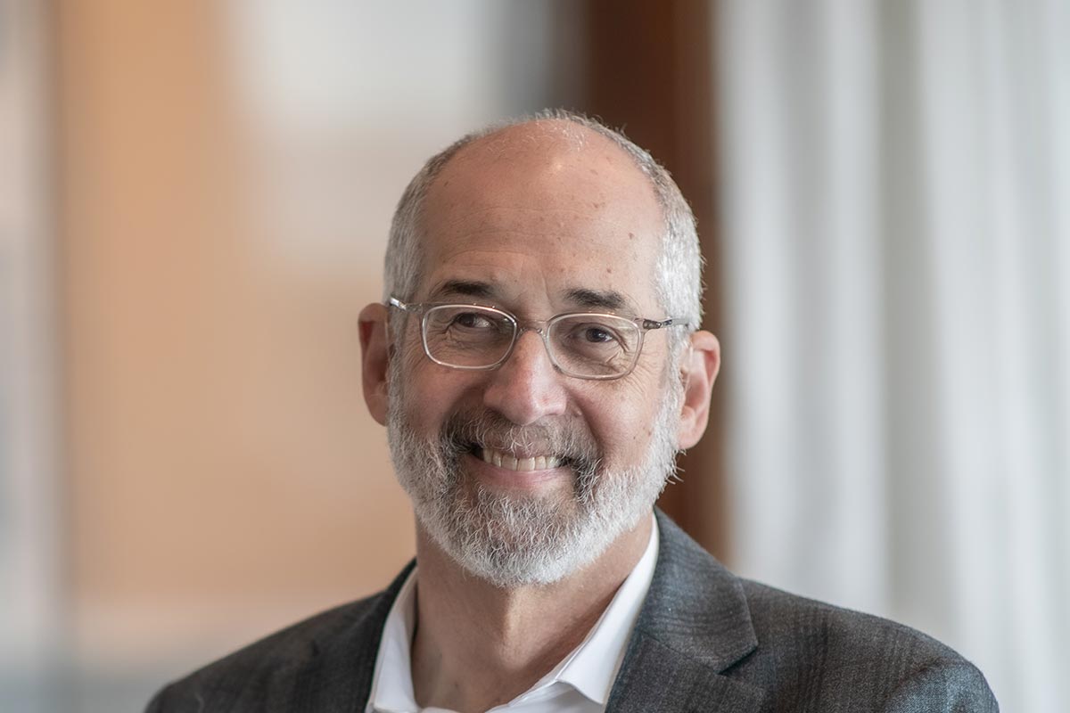 Jon Rollins, Principal at GFF, close-up portrait with glasses, beard, and suit jacket, photographed in a modern office background.