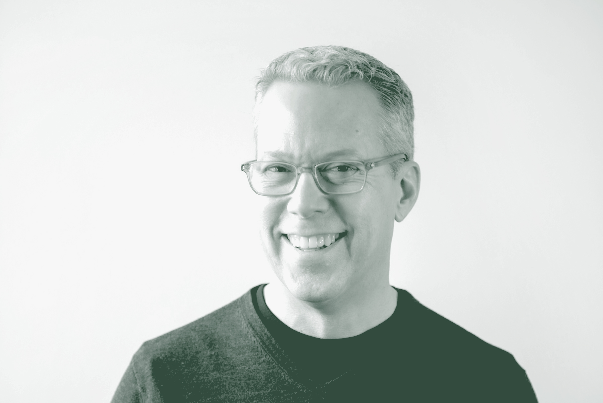 A black and white portrait of Russell Hagg, an Associate Principal and Senior Interior Design Leader with GFF in the Interior Design Studio, in front of a white background.