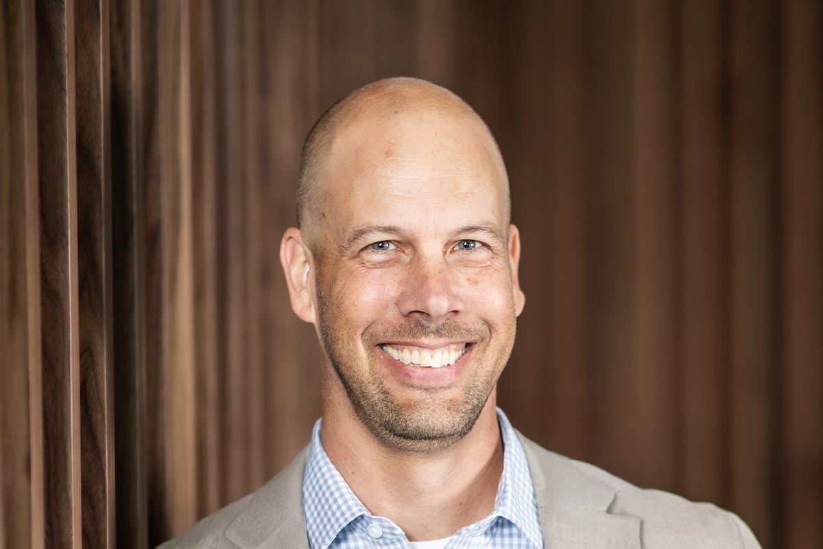 Aaron Hunt, AIA, Managing Director of GFF Fort Worth and Denver, close-up professional portrait with a wood-paneled office wall backdrop.
