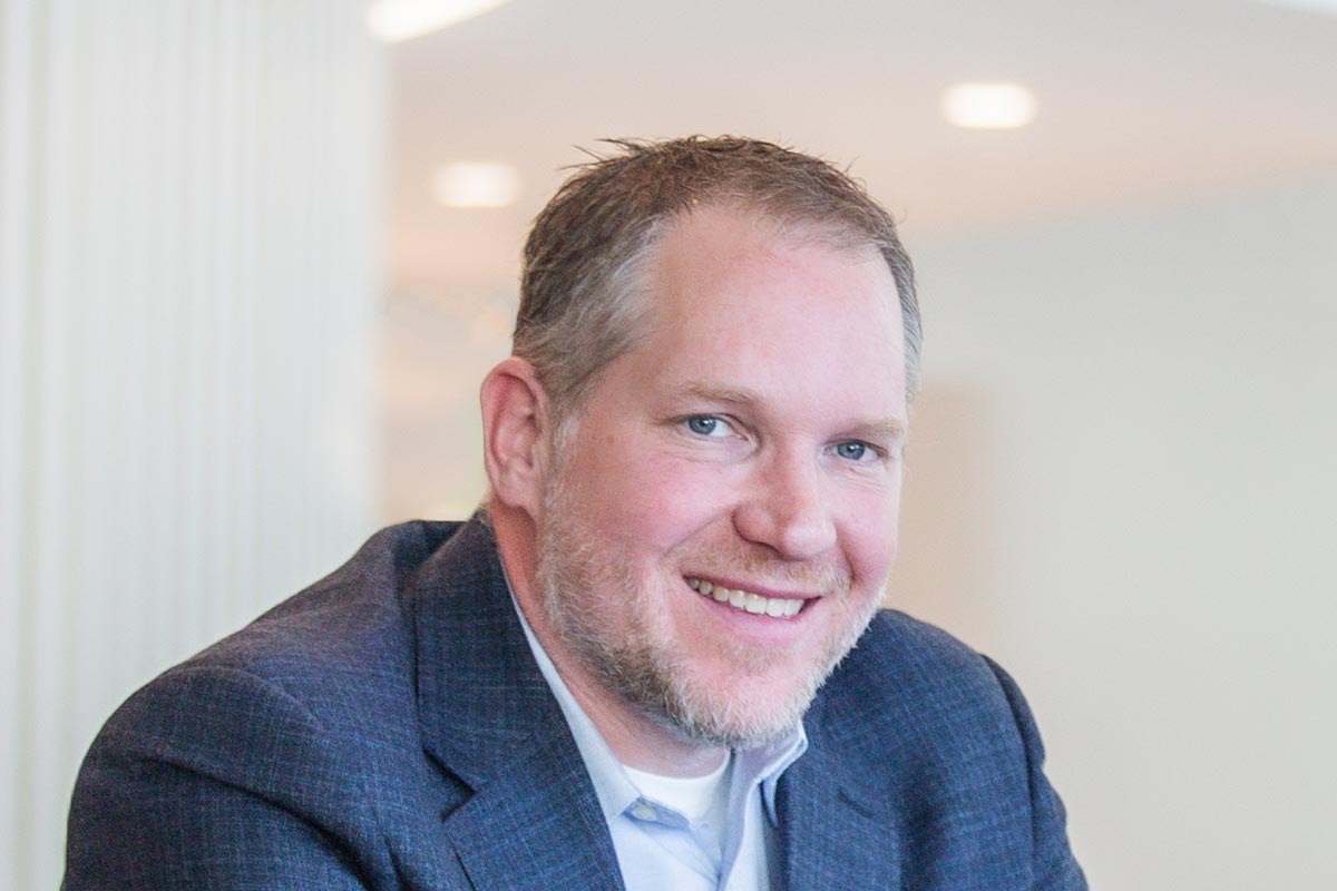 Andrew Adkison, Senior Design Leader and architect at GFF in Dallas, smiling in a modern workplace interior.