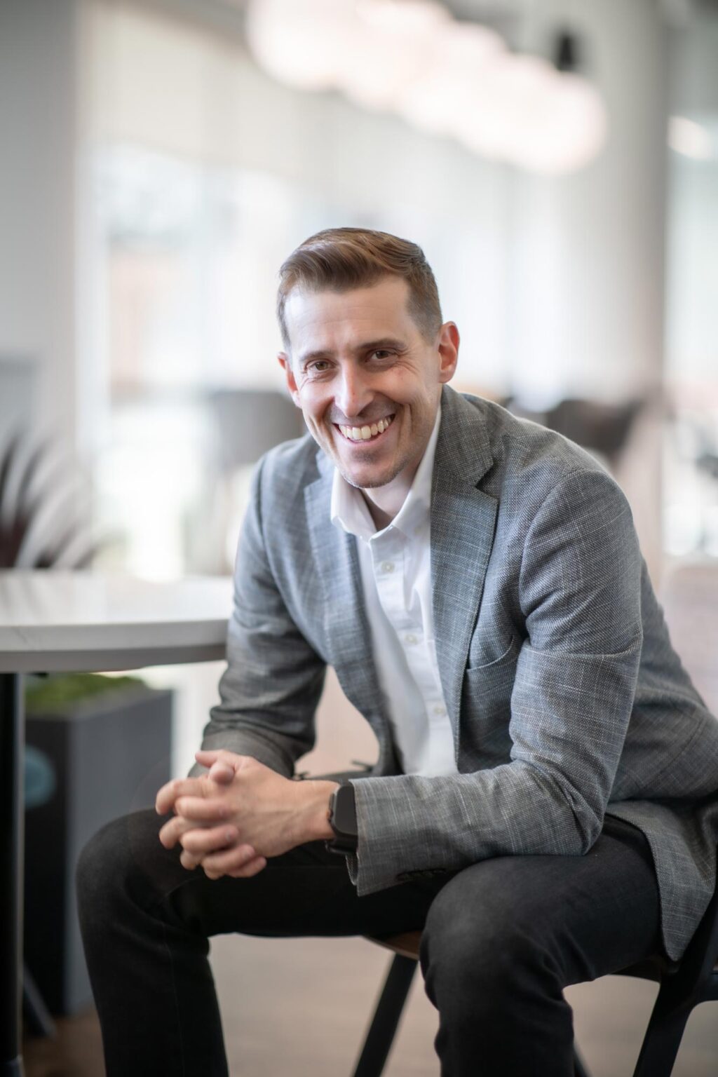 Jason Cave, Associate Principal at GFF, seated at a round table in a bright office, smiling and wearing a gray blazer and white shirt.