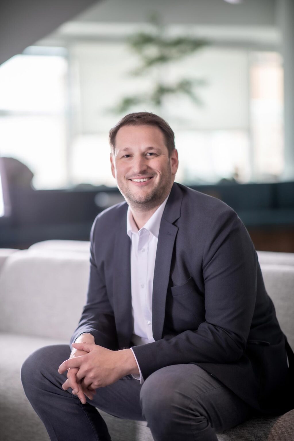 Jeremy Roehr, AIA, NCARB, Associate Principal and Studio Director at GFF, seated on a sofa in a dark blazer and white shirt, smiling in a modern office.