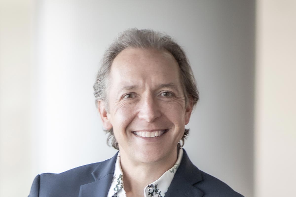 Close-up portrait of Michael Lehr smiling warmly in natural light, wearing a navy jacket and patterned shirt.