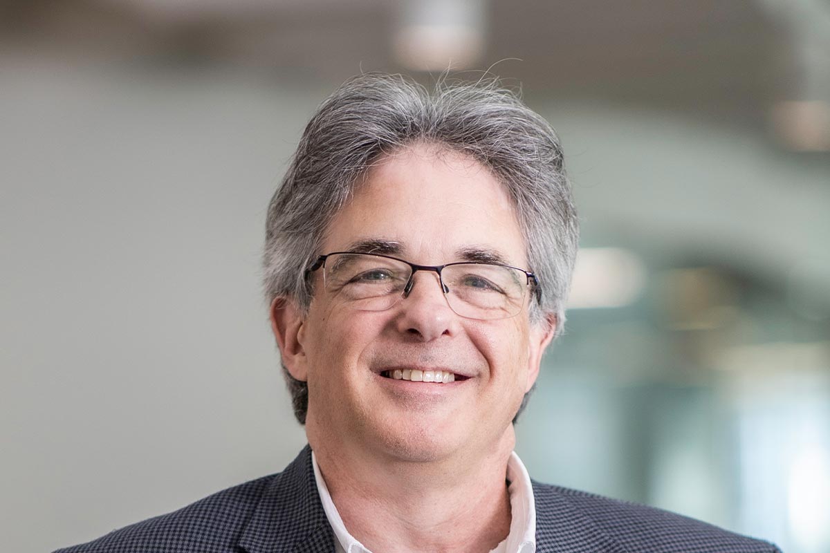 A cropped landscape portrait of Scott Kanaga, Associate Principal and Studio Director at GFF, smiling in front of a softly lit office background.