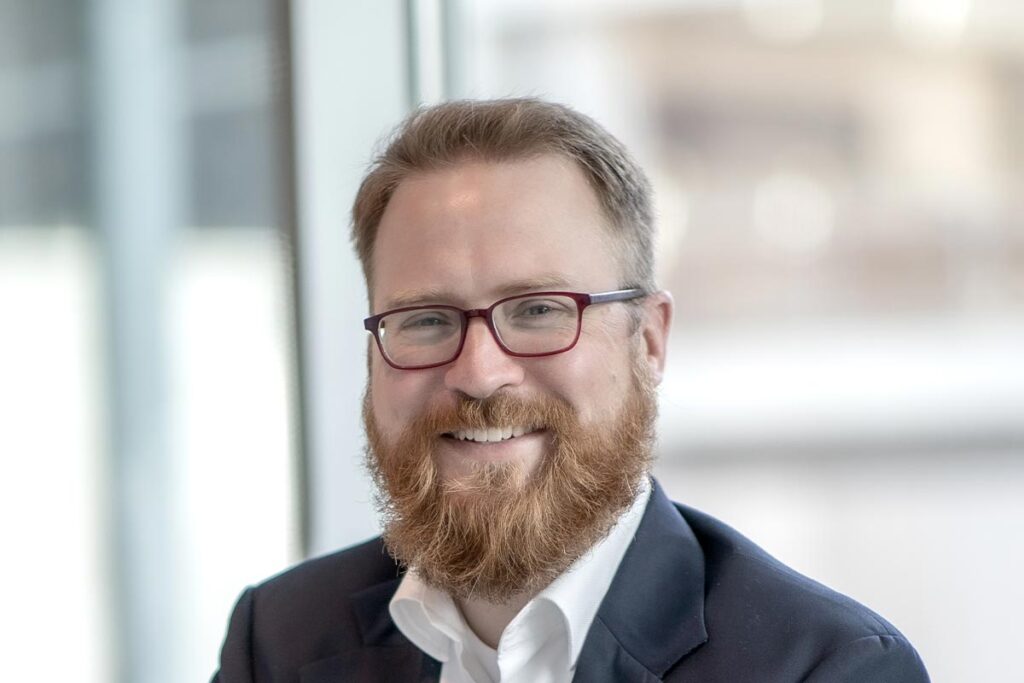 A cropped landscape portrait of Sam Stribling, Associate and Studio Director at GFF, smiling in a light-filled office interior.