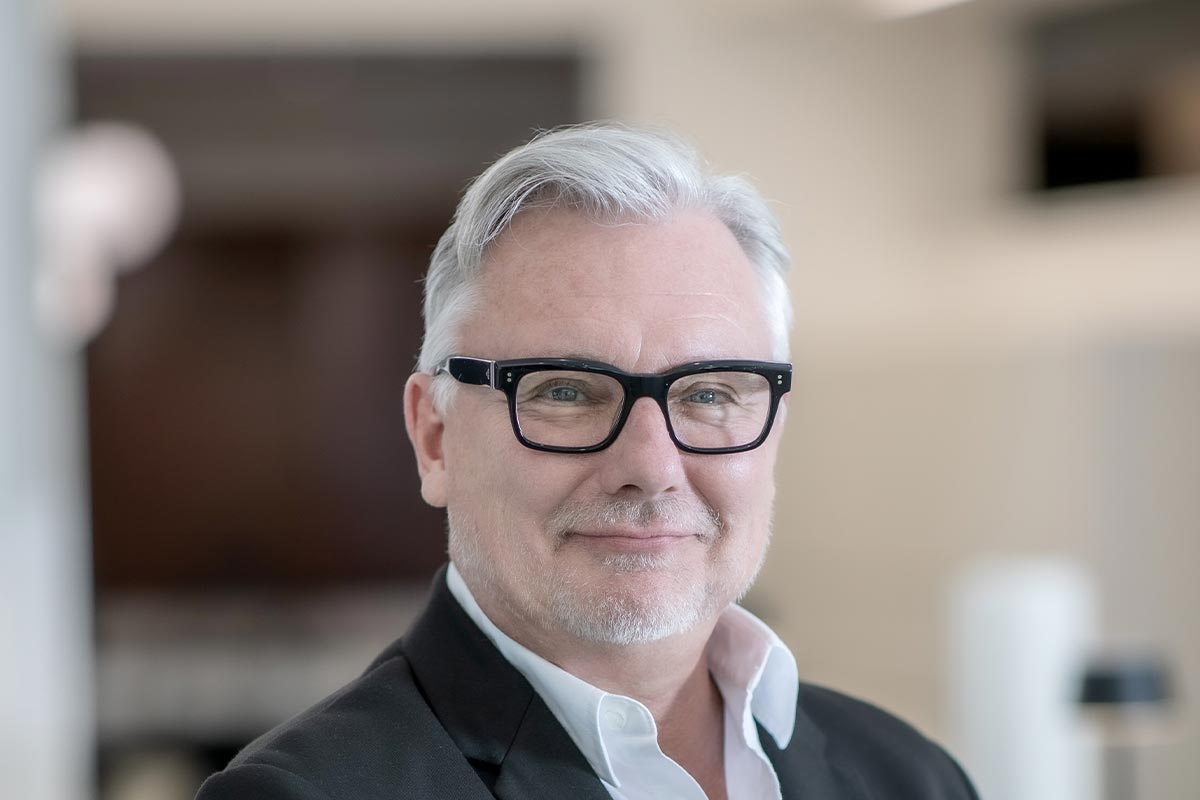 A cropped landscape portrait of Chris Andersen, Associate Principal and Senior Project Leader at GFF, smiling in a softly lit interior setting.