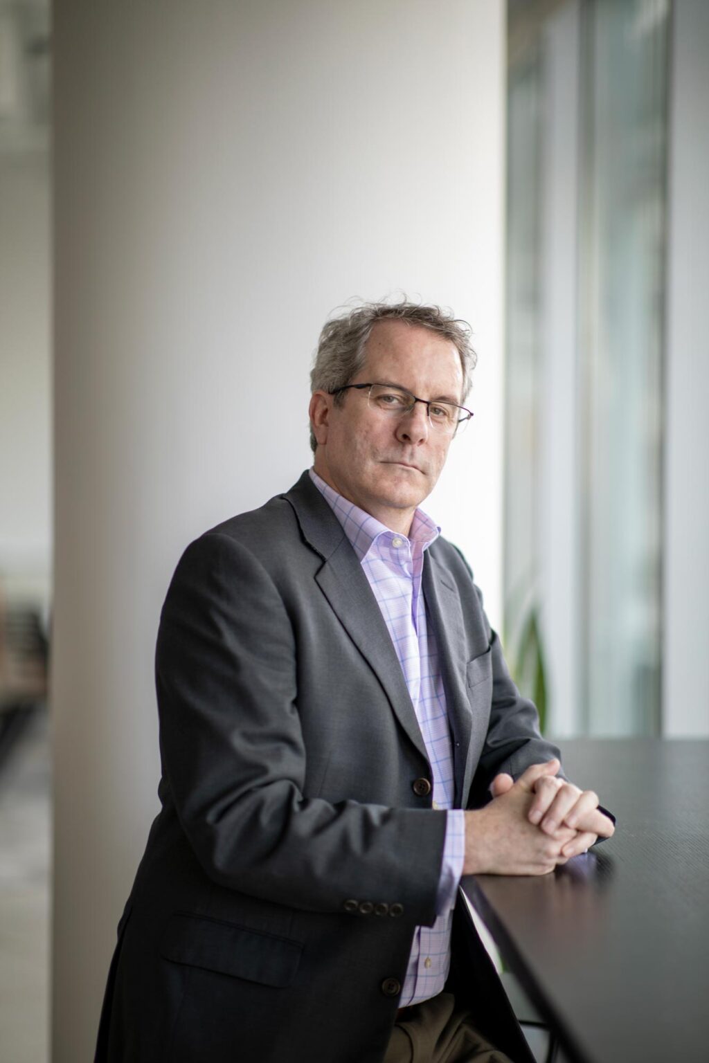 David Boone, Associate Principal and Senior Interior Design Leader at GFF, seated by a window wearing a gray blazer and light purple checkered shirt.