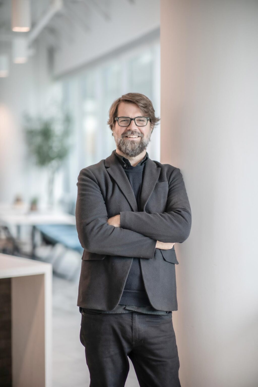 Mark Holsinger, Associate Principal and Senior Design Leader at GFF, standing with arms crossed against a column in a modern office interior, wearing a dark jacket and glasses.