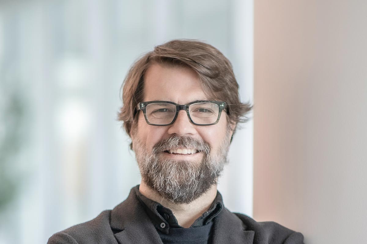 Mark Holsinger, Associate Principal and Senior Design Leader at GFF, close-up professional portrait with glasses and beard, photographed in a modern workplace environment.