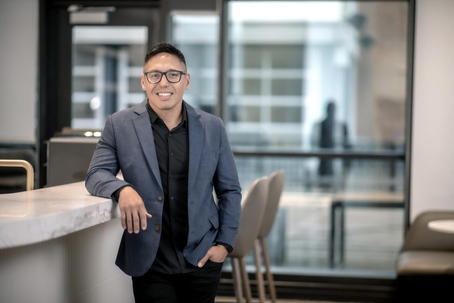 Lance Abaya, Senior Design Leader at GFF, standing at a marble countertop in a modern office wearing a navy blazer and black shirt.
