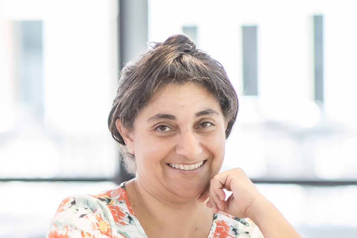 A cropped landscape portrait of Nardine Mansi, Associate and Senior Project Leader at GFF, smiling in a softly lit office interior.