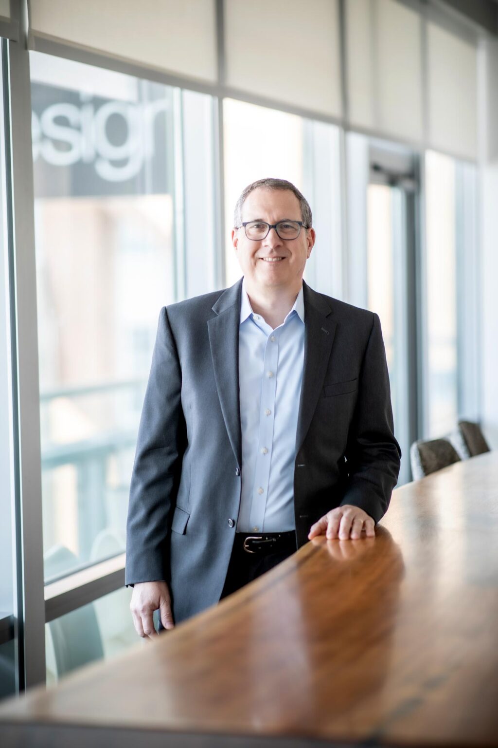 A portrait of Steve Brookover, Associate and Senior Design Leader at GFF, standing beside a wooden conference table in a light-filled office.