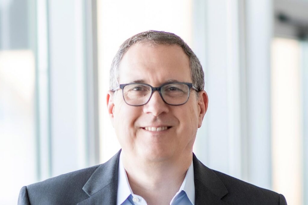 A cropped landscape portrait of Steve Brookover, Associate and Senior Design Leader at GFF, smiling near a window in a softly lit office environment.