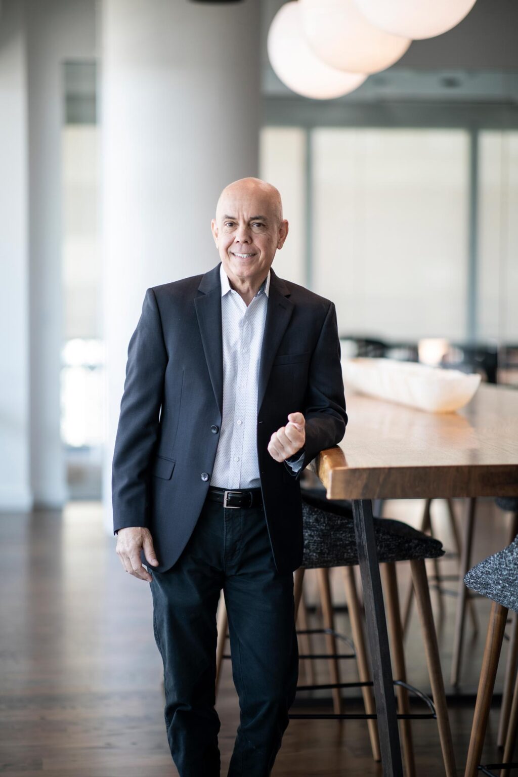 Harrison Connor standing beside a tall wood table in a modern office space, wearing a dark blazer and light collared shirt.