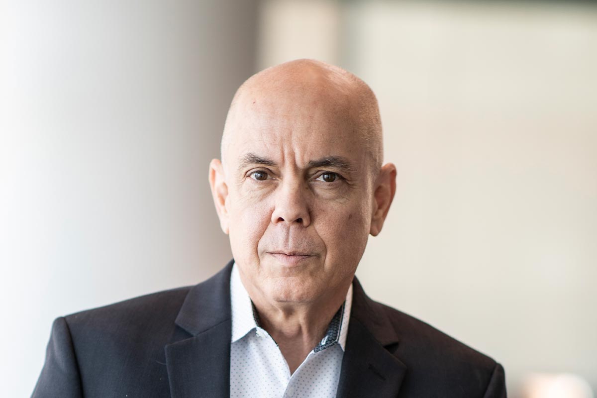 Close-up portrait of Harrison Connor in a dark blazer and light shirt, with a softly blurred interior background.