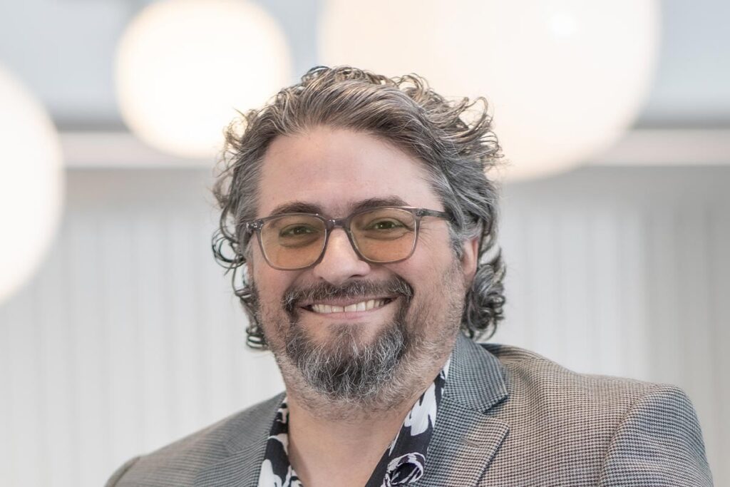Loren Boynton, Senior Project Leader at GFF, close-up portrait with glasses and patterned shirt under a gray jacket.