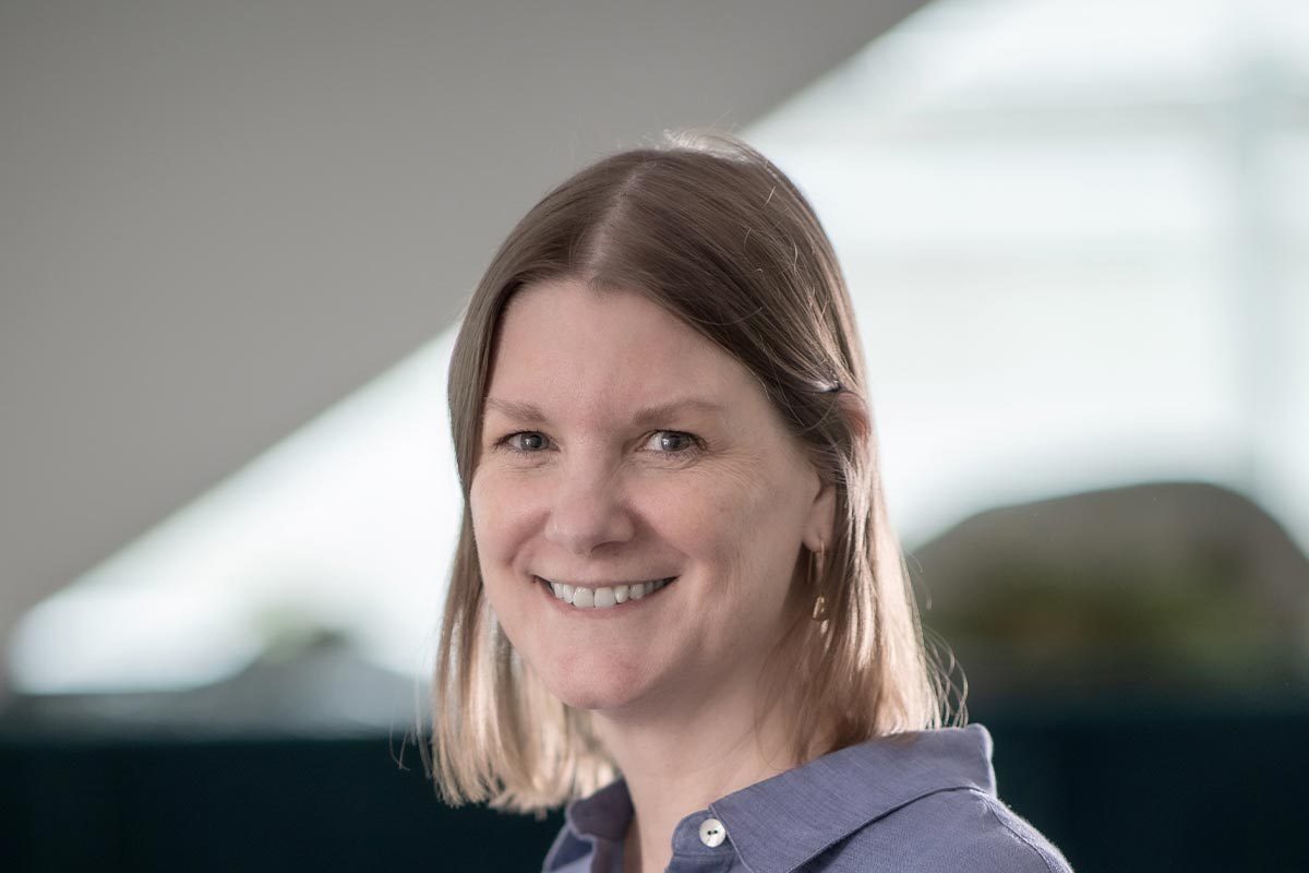 Sandra Beer, Senior Project Leader at GFF, close-up professional portrait in a blue blouse with soft daylight and blurred office background.