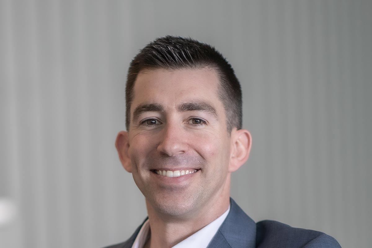 A cropped landscape portrait of Adam Fenner, Project Leader at GFF, smiling in a softly lit modern office environment.