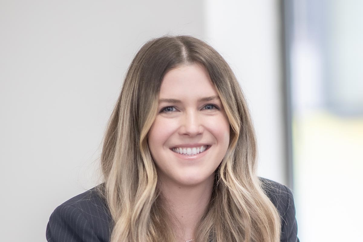 A cropped landscape portrait of Jenna Ross, Interior Design Leader at GFF, smiling in a softly lit modern office.