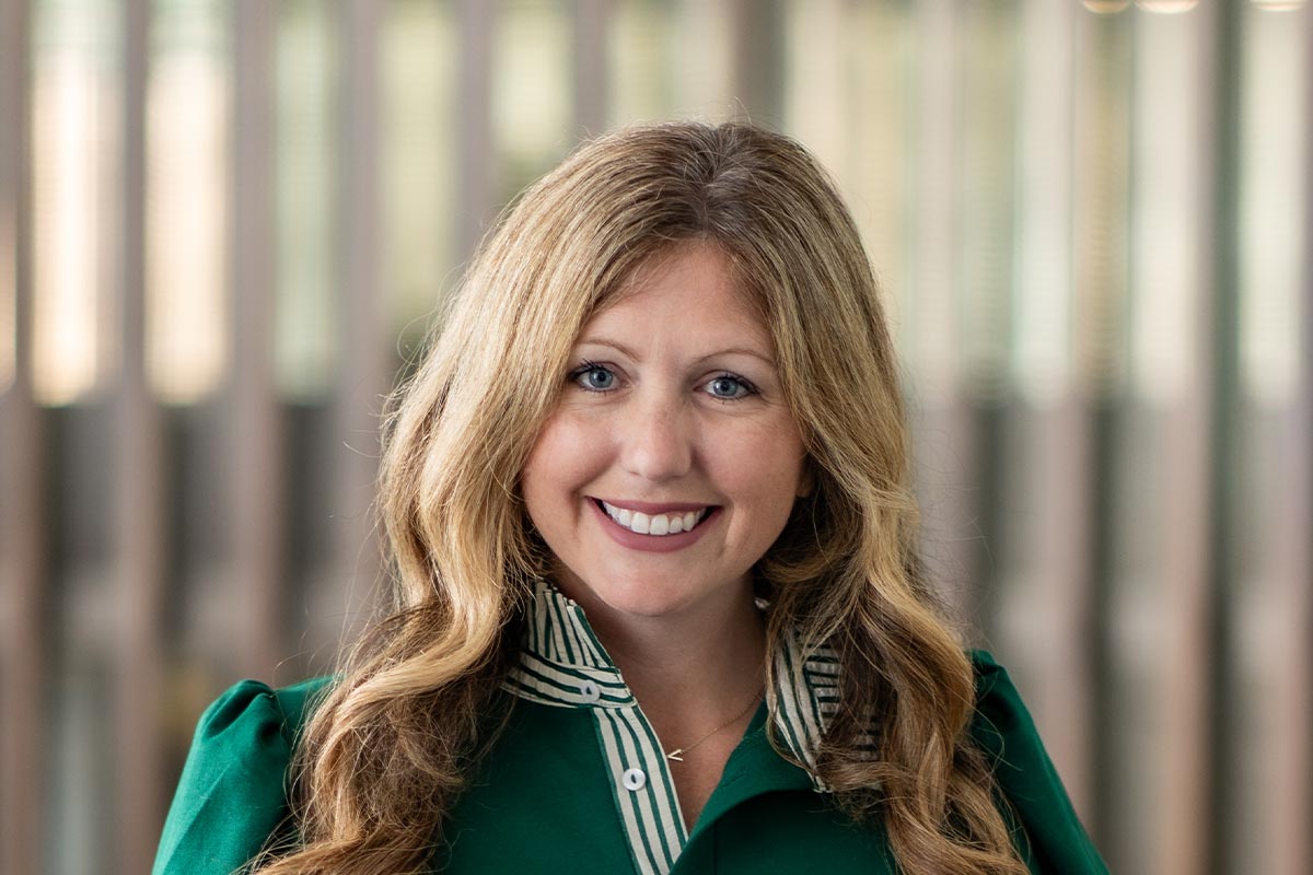 Close-up portrait of Reagan Compton smiling in front of a softly blurred vertical wood panel background.