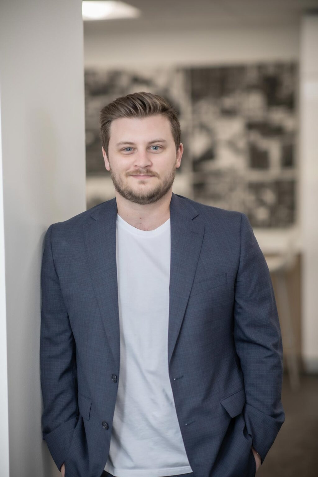 Zach McLain, Design Leader at GFF’s Austin studio, standing against a wall wearing a blue blazer and white shirt in a modern office setting.
