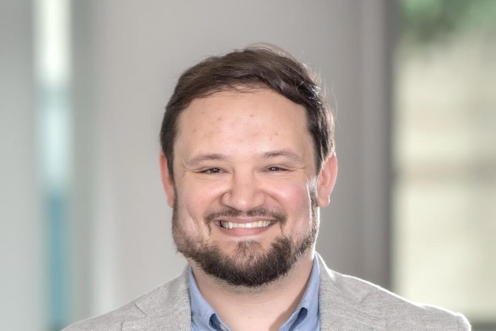 A cropped landscape portrait of Jacob Thibodeaux, Senior Project Coordinator at GFF, smiling in front of a softly blurred office background.