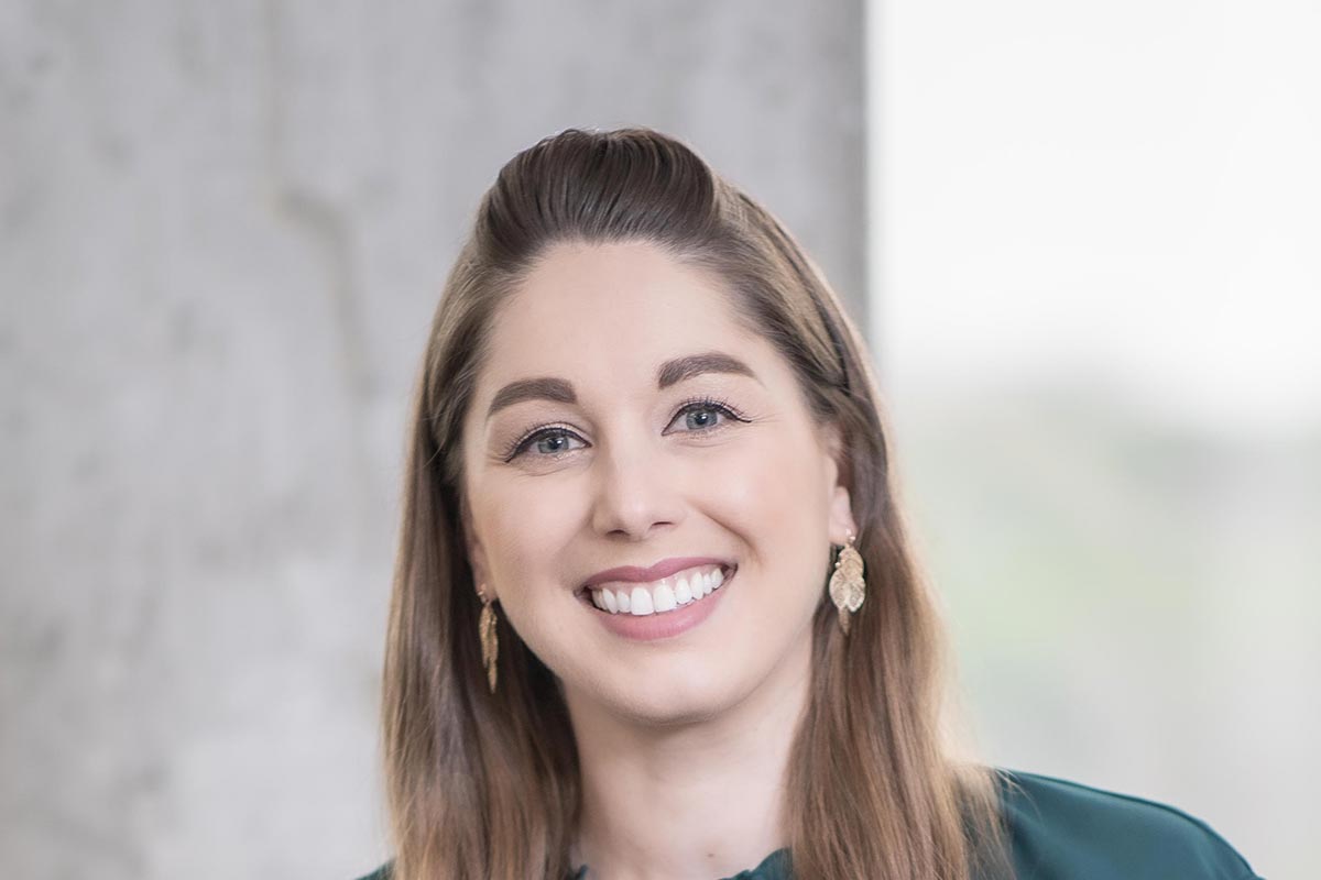 Katie Myers Wender, Senior Interior Design Coordinator at GFF, close-up portrait with long brown hair and gold leaf earrings, photographed in a professional office setting.