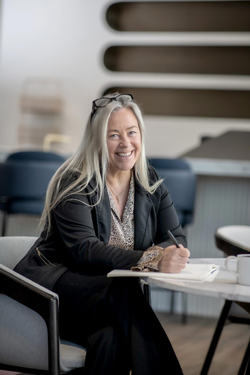A portrait of Lena Starostine, Senior Project Coordinator at GFF, seated at a table with a notebook, smiling in a contemporary office setting.