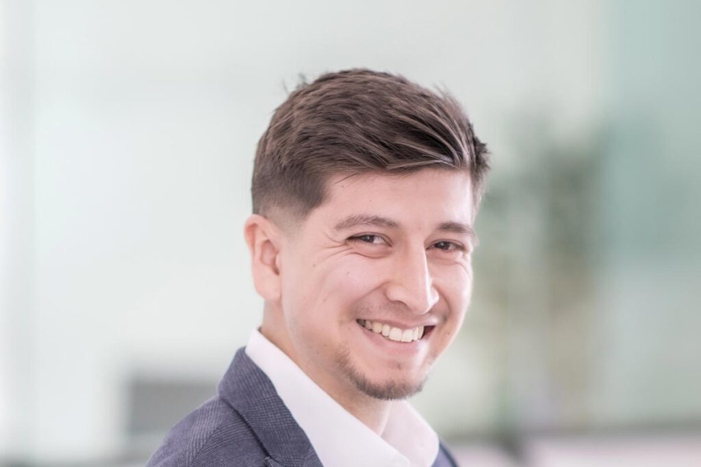 A cropped landscape portrait of Roberto Oviedo, Senior Project Coordinator at GFF, smiling in front of a softly lit office background.