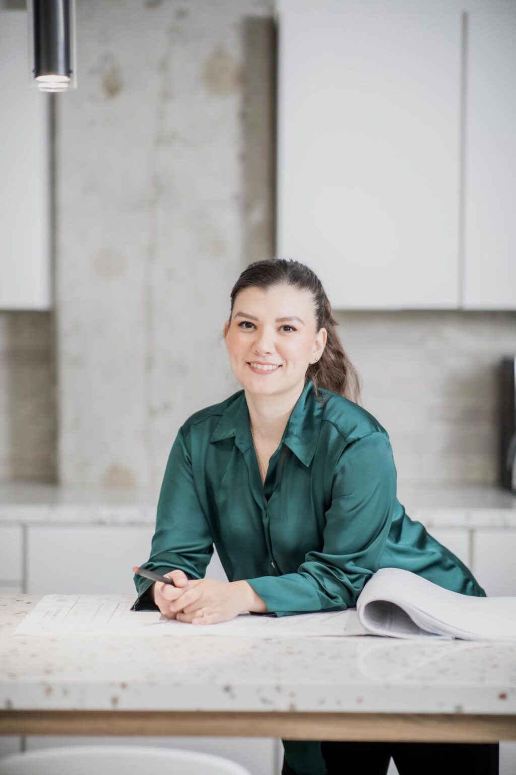 Cecilia Garcia leaning on a terrazzo table in a bright modern office interior, wearing a green blouse and smiling.