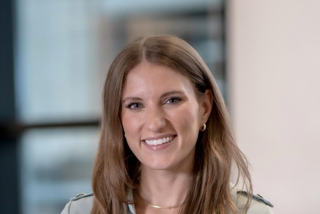 Emily Carvell, Marketing Coordinator at GFF, close-up smiling portrait in a light green dress with blurred office background.