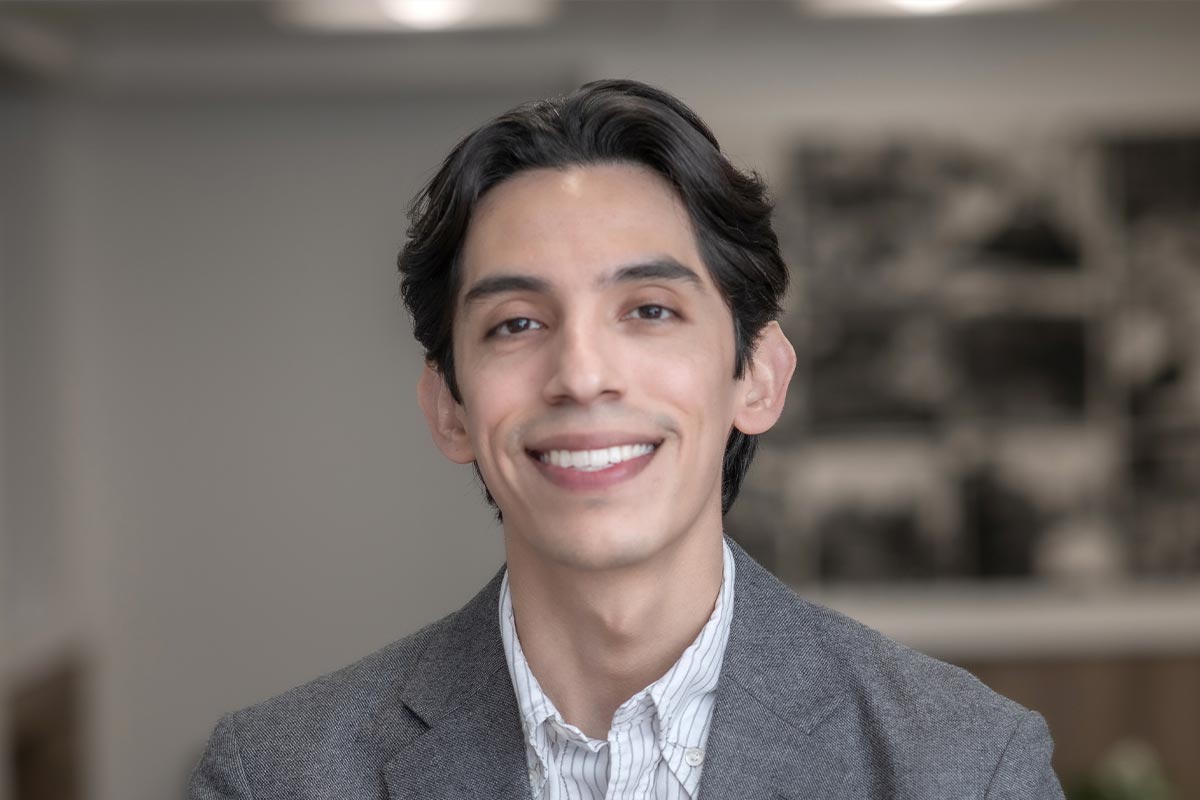 Close-up portrait of Woody Owens wearing a gray jacket and striped shirt, in front of a neutral office backdrop.