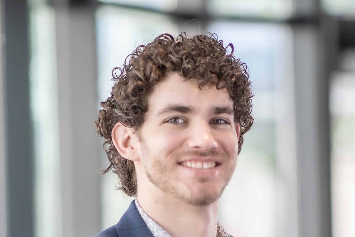 A cropped landscape portrait of Jonathan Moebius, Design Professional at GFF, smiling in front of a softly lit modern office background.