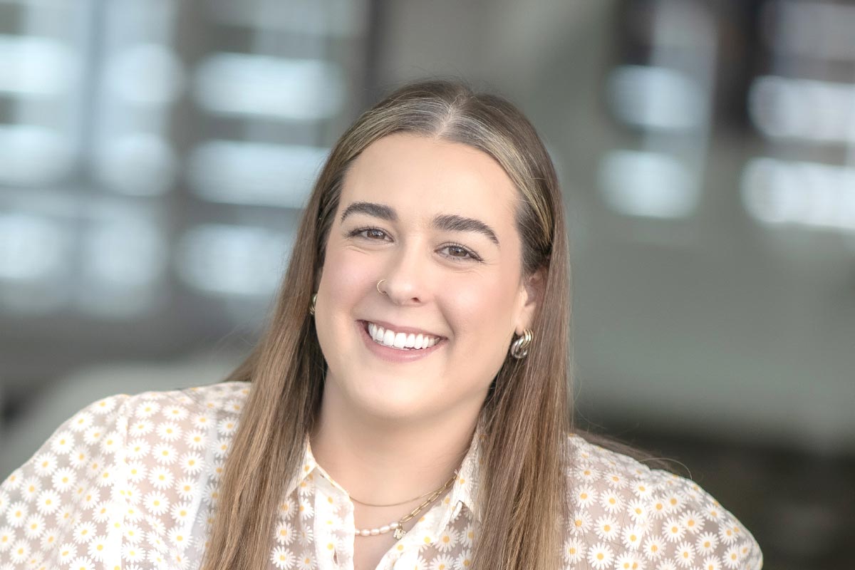 Maya Pavon, Design Professional at GFF, close-up portrait with long straight hair and subtle jewelry in soft daylight.