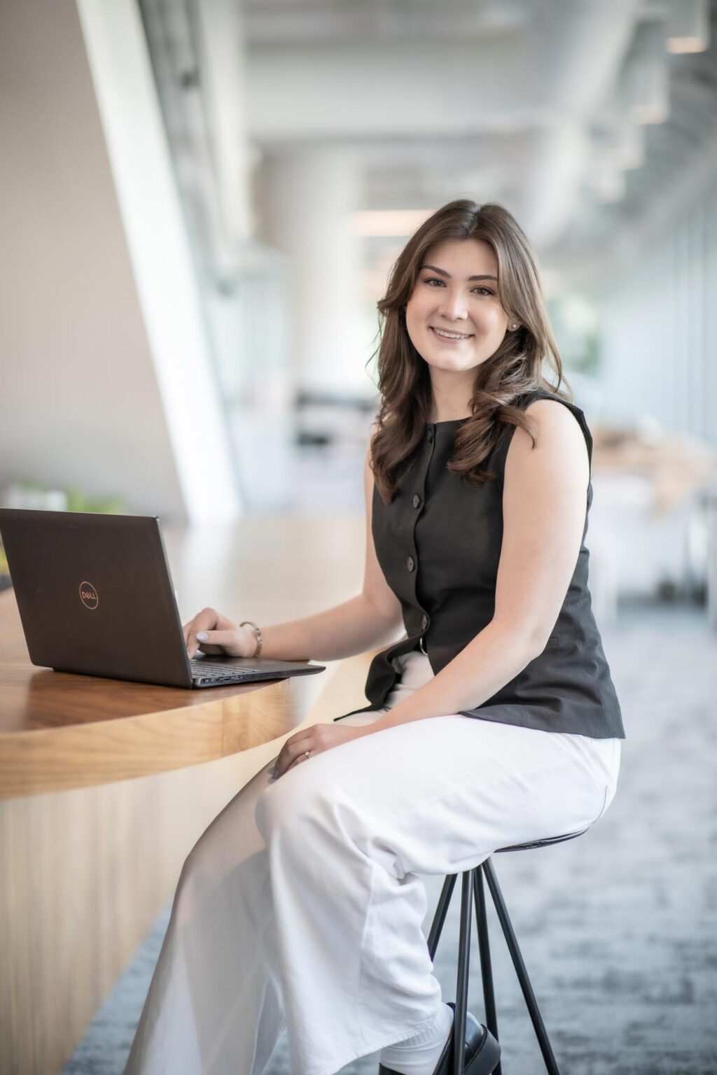 A portrait of Natalie Hummell, Architectural Professional at GFF, seated at a wood table with a laptop in a bright office interior.