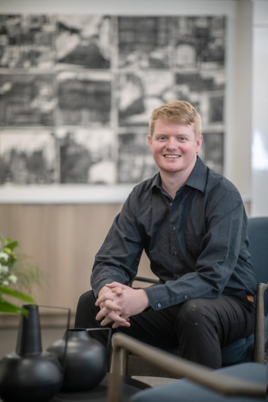 Robin Hatherill seated in a modern office interior with artwork in the background, wearing a dark shirt and smiling.