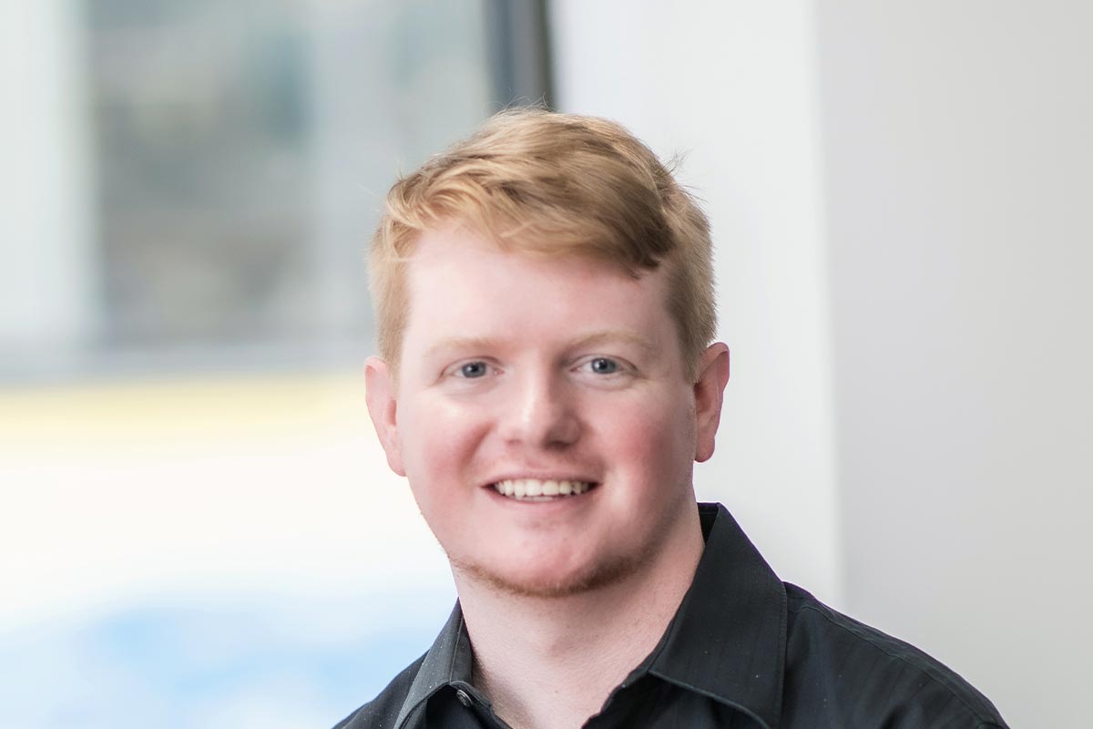 Close-up portrait of Robin Hatherill wearing a dark shirt, smiling in front of a softly lit background with window light.