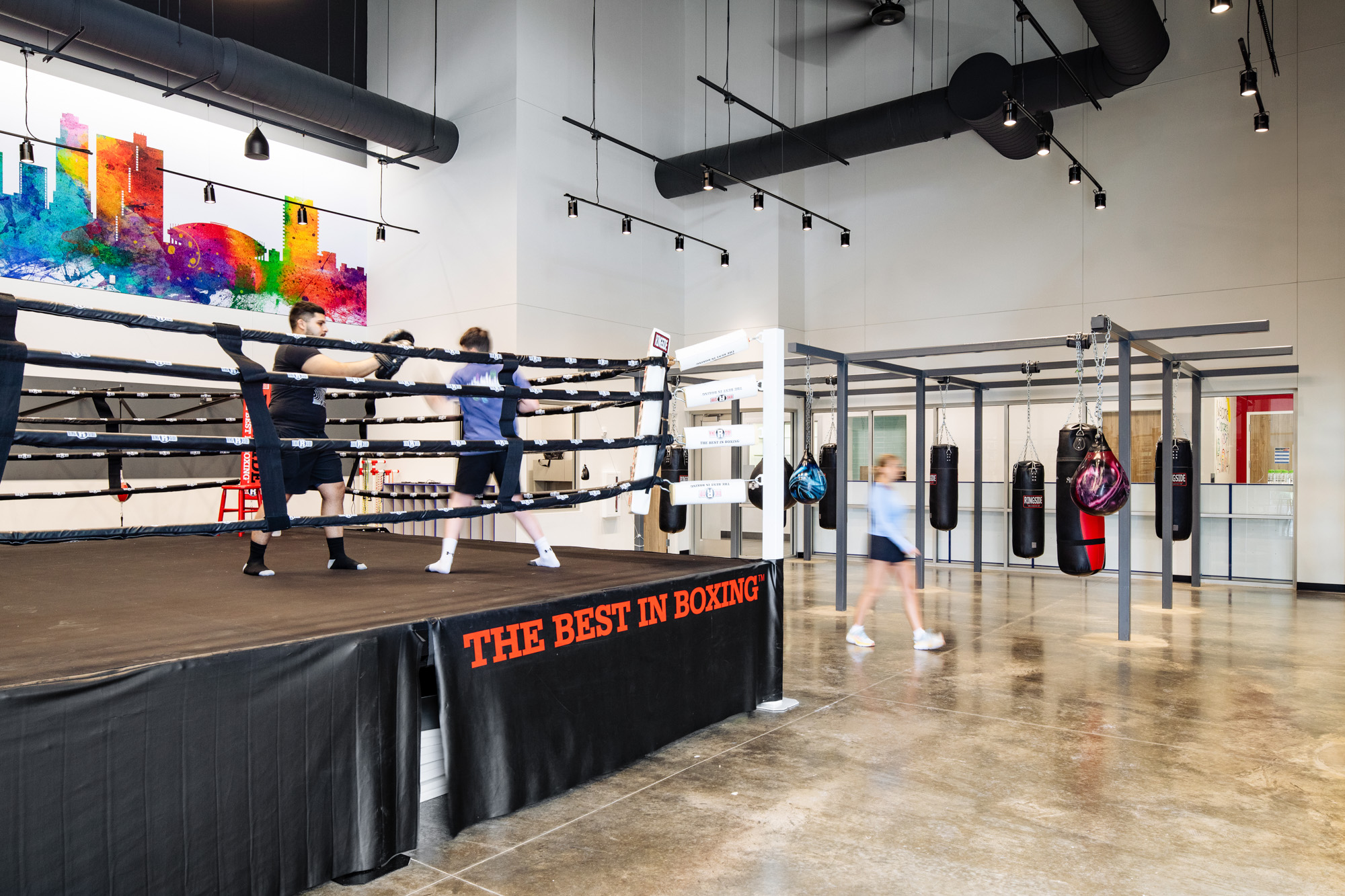 Two individuals sparring in a boxing ring inside the Diamond Hill Community Center, with vibrant, colorful artwork on the wall in the background.