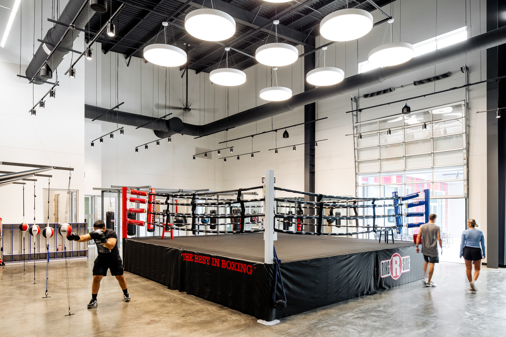 A wide view of a boxing ring and surrounding fitness equipment in the Diamond Hill Community Center, illuminated by modern circular lighting fixtures.