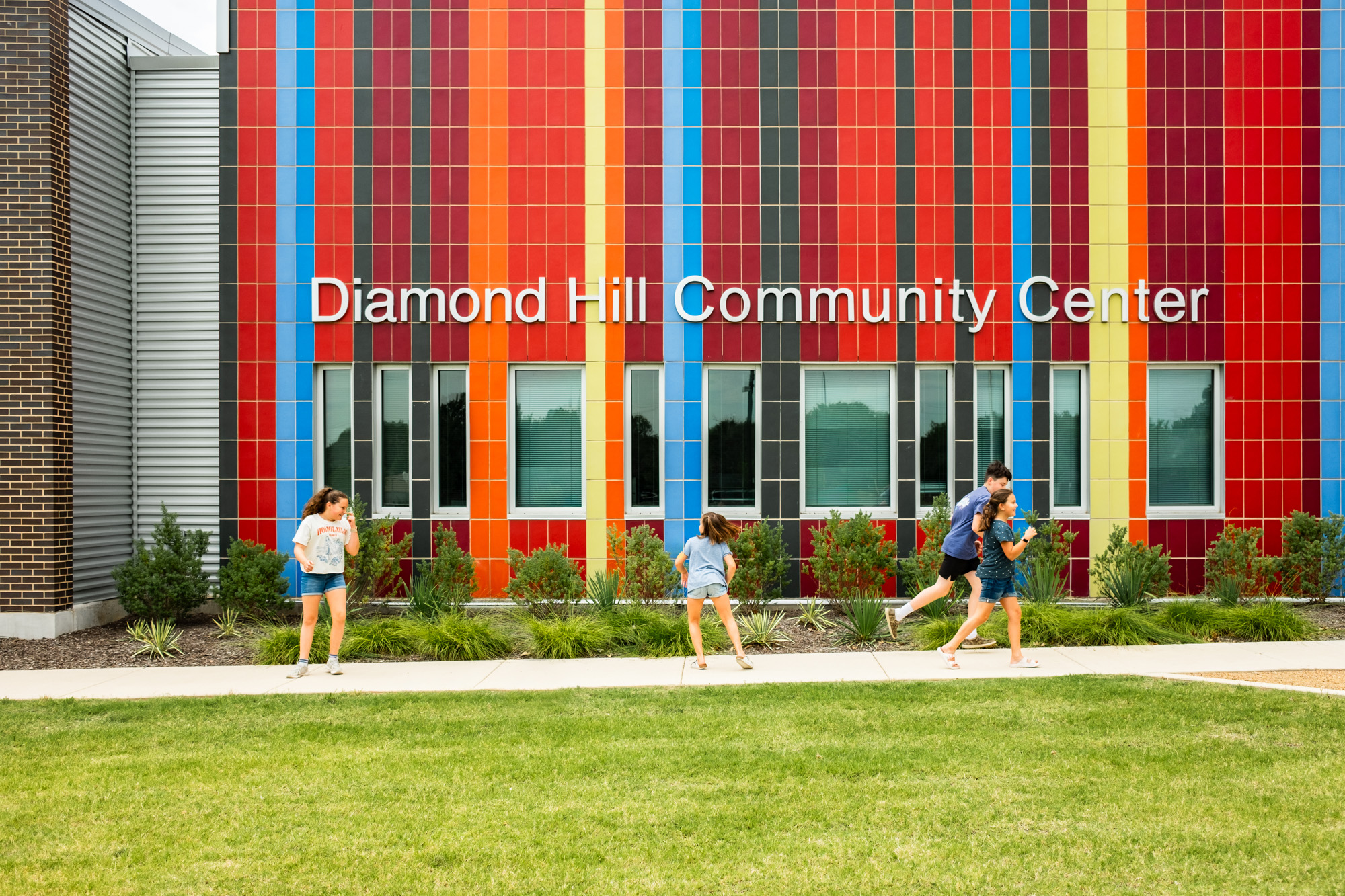 The colorful glazed block facade of the Diamond Hill Community Center, with children playing on the grass in front.